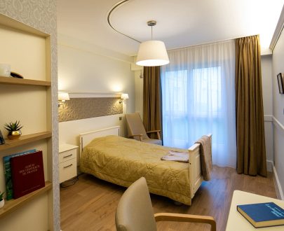 Chambre individuelle avec coin bureau, étagères, fauteuil, raye de porte malade au plafond
